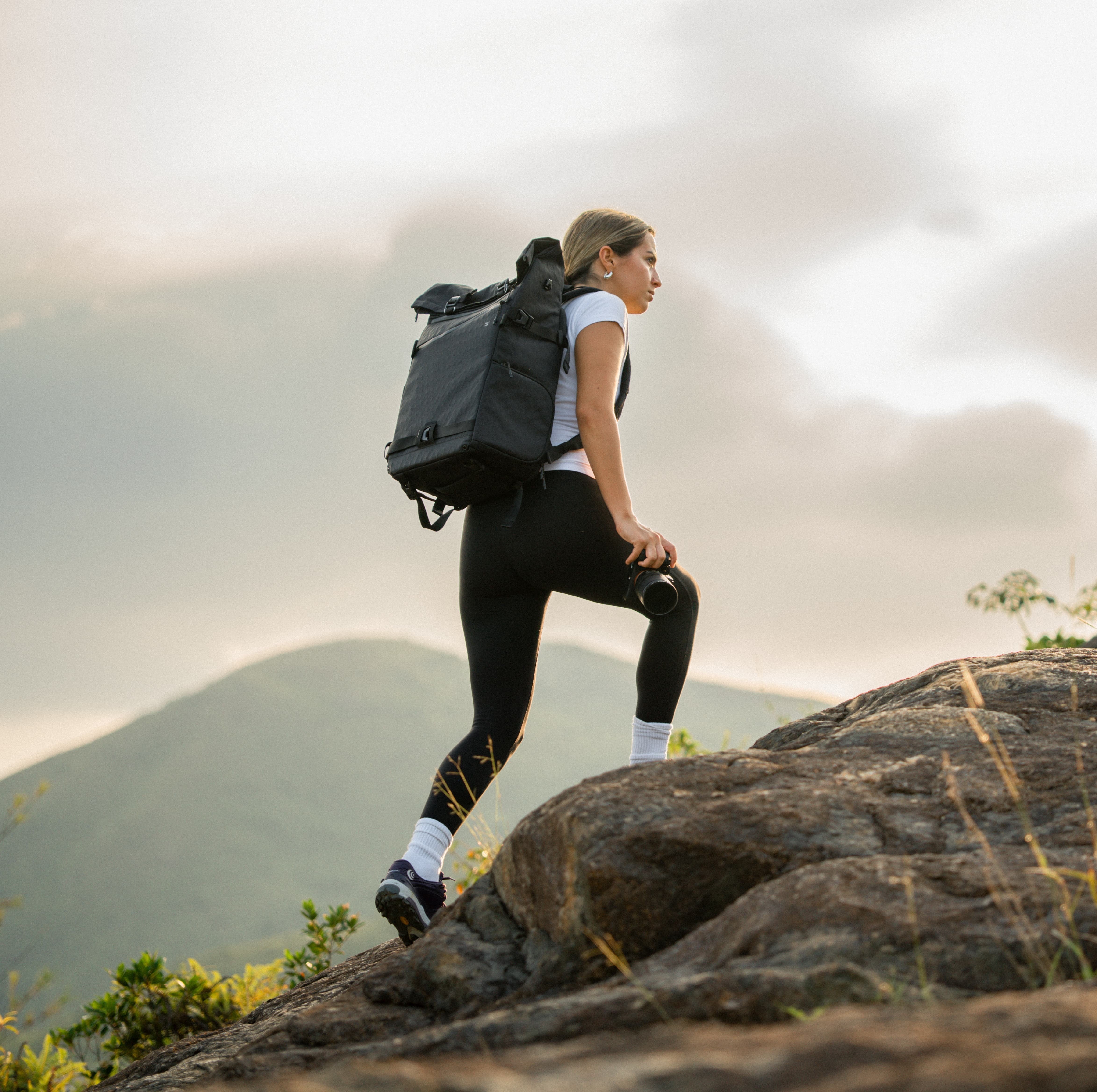 woman with camera backpack climbing mountain