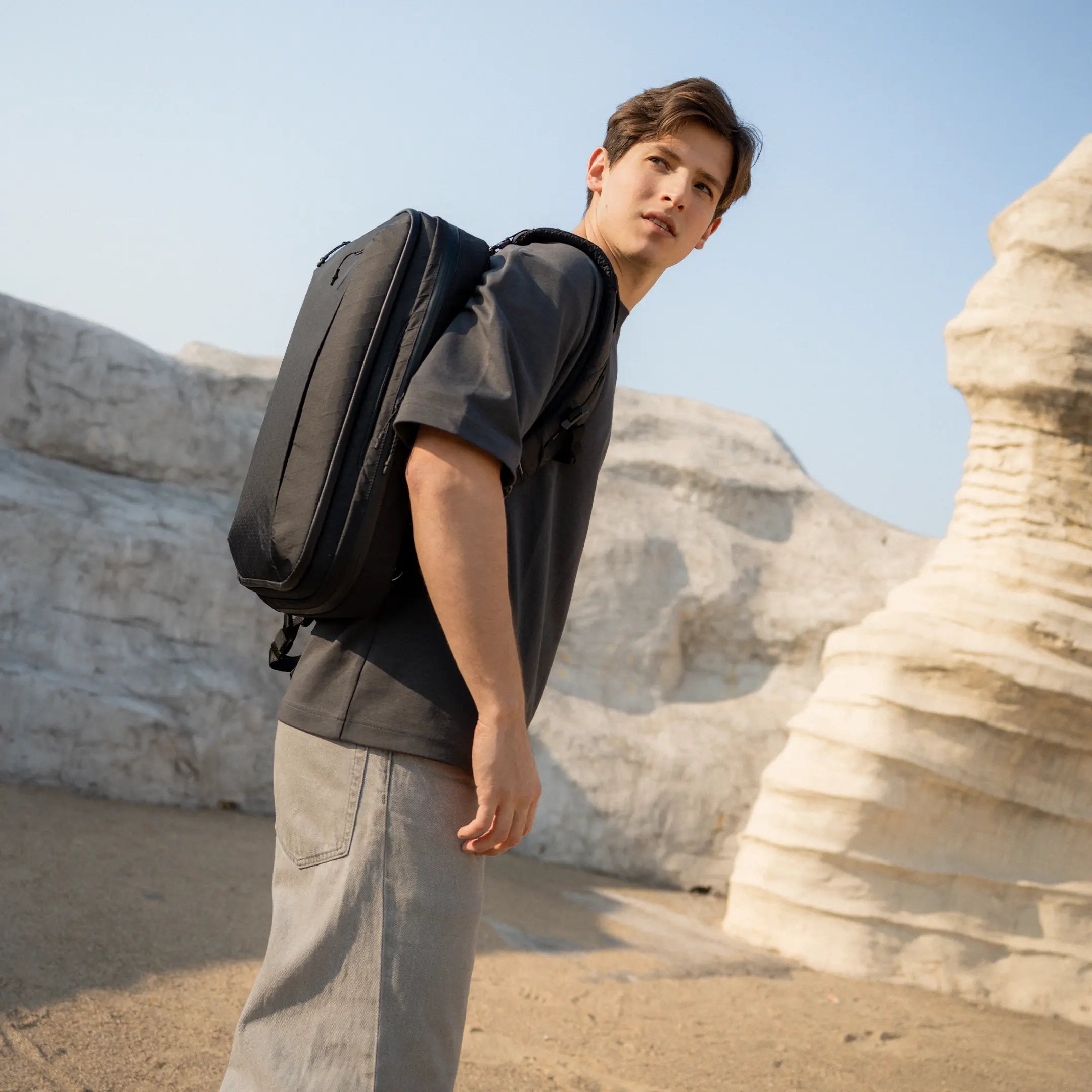 Person with a black backpack standing in a desert landscape with rock formations.