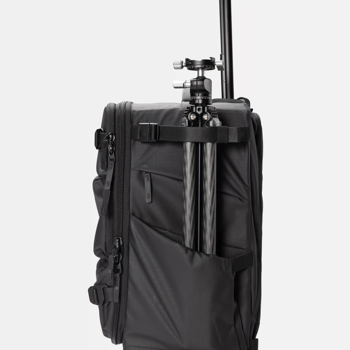 A black soft-sided travel or camera bag with a tripod mounted vertically inside a side pocket, shown against a plain light gray studio background.