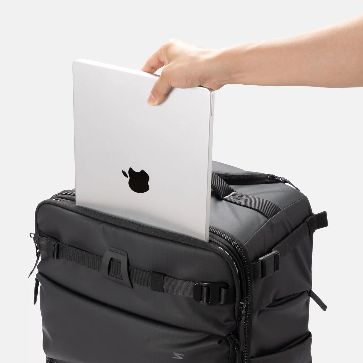 A black laptop bag with a hand inserting a silver laptop into its top slot, shown against a clean white background.