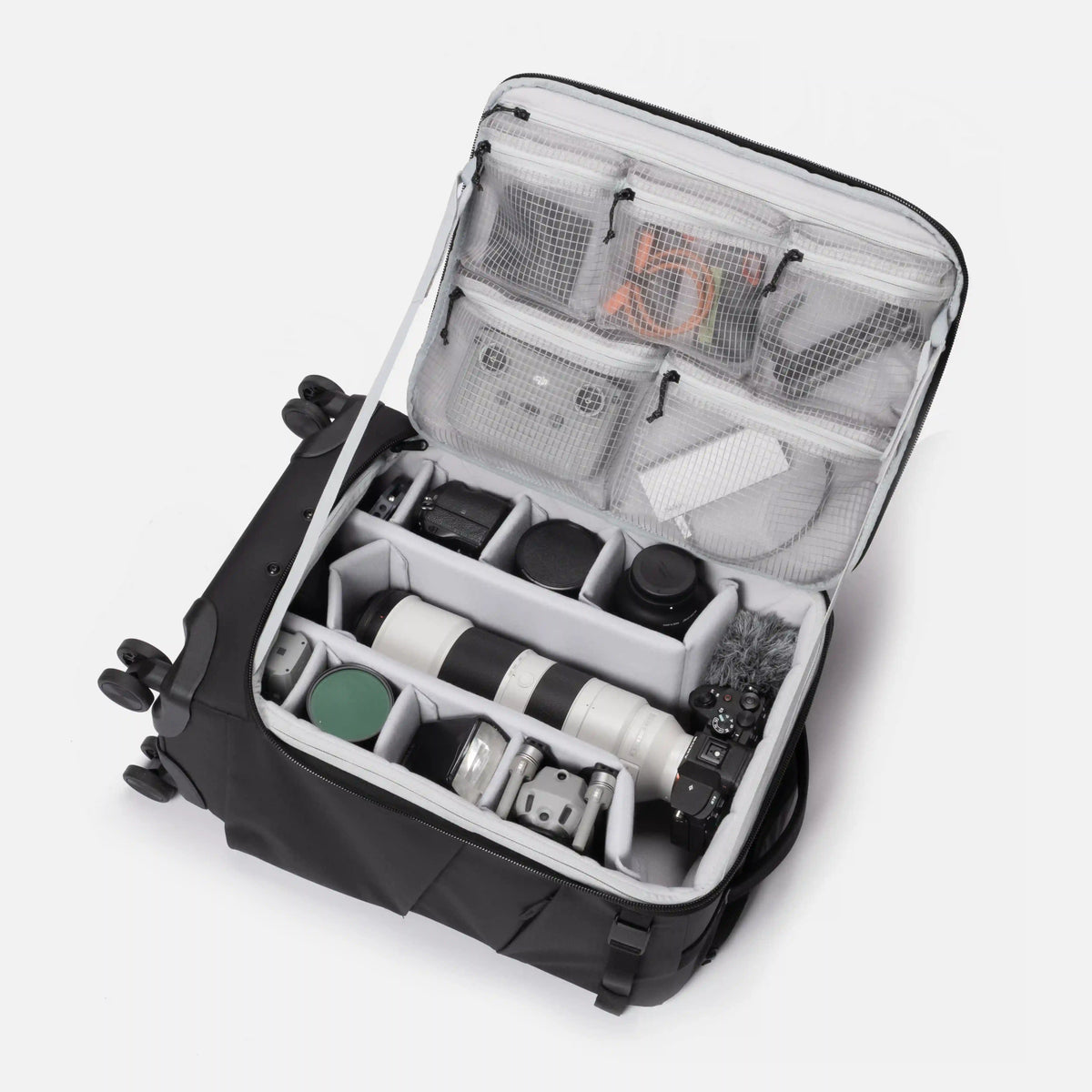An open black and gray camera gear organizer suitcase shown from a top-down angle, filled with camera equipment including a telephoto lens, camera body, and accessories in mesh and foam compartments.