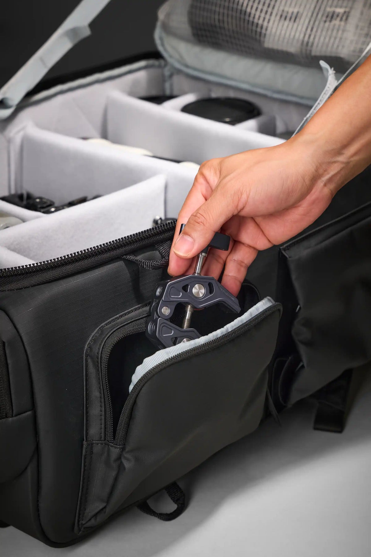 A close-up of a person's hand inserting a black camera lens protector into a zippered compartment of a black camera bag with white foam inserts.