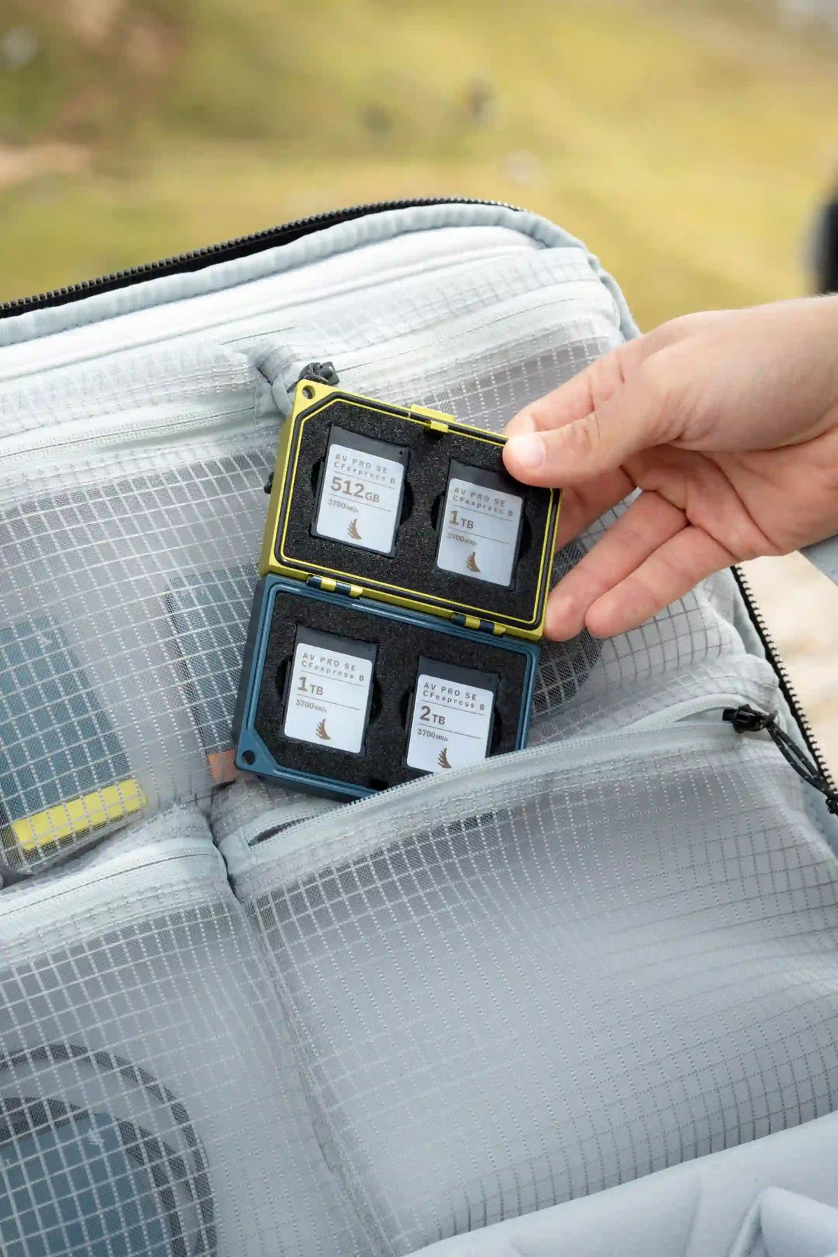 A hand holding a small black and yellow card case containing three small cards, placed inside a gray mesh organizer pouch of a larger bag.