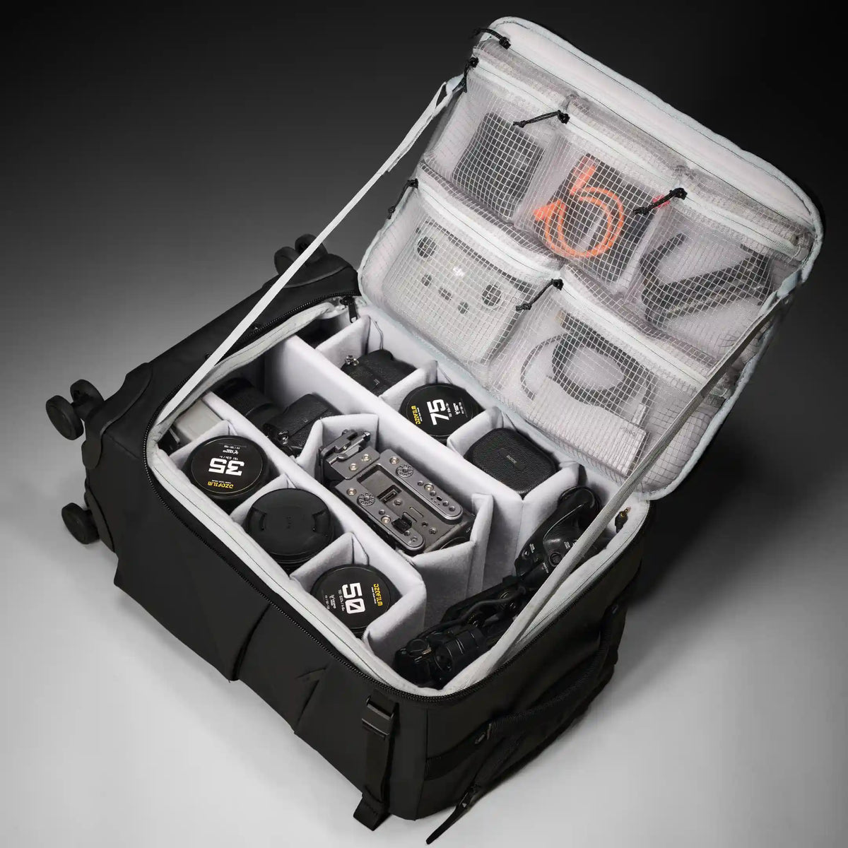 A close-up of a zippered travel organizer bag with multiple white mesh pockets and black zipper pulls, shown against a dark gray studio background.