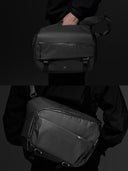 Black camera sling bag held by a person against a dark background