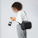 Person holding a black backpack and a camera with a white background