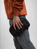 Person wearing an orange jacket holding a compact black Sakk Gear pouch with straps