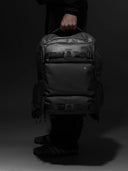Person holding a black backpack against a dark background