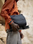 Person holding a black bag with camera equipment against a blurred natural background