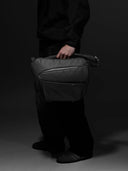 Person holding a black camera bag against a black background