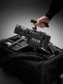 Hand holding a RED camera over a black carrying case on a gray background