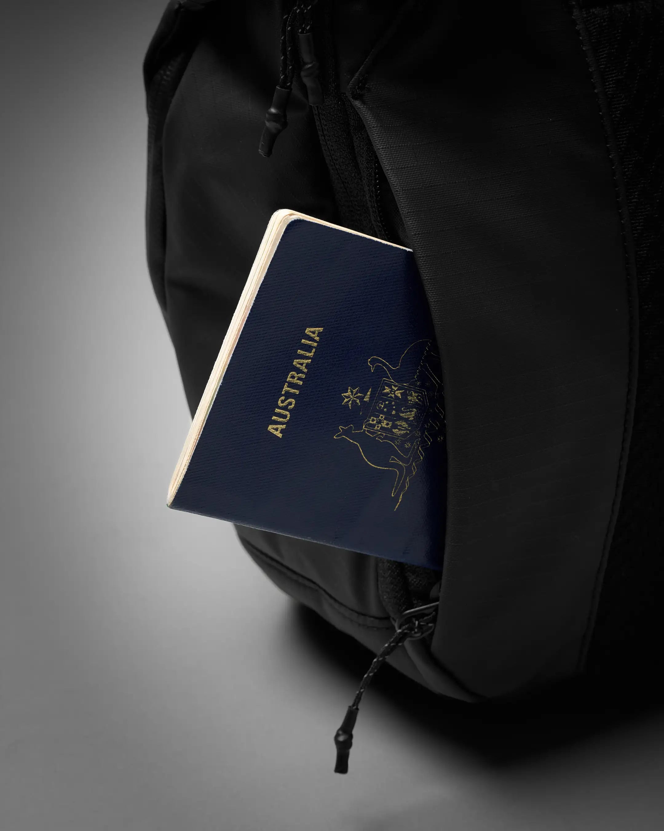 Black backpack with an Australian passport peeking out from a pocket on a gray background