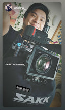 Instagram story screenshot of a smiling man on set with a large cinema camera mounted on a Sakk Gear support bag; text overlay credits @andew_ and @sakk.global