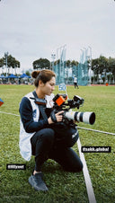 Social media photo of a woman kneeling on a sports field using a Sakk Gear bag to stabilize a professional camera with long lens