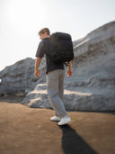 Dynamic shot of a man walking on pavement with a large black backpack, with blurred motion and rocky background