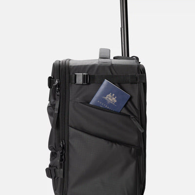 A black rolling suitcase with an extended telescoping handle, featuring a side utility pocket holding a passport.
