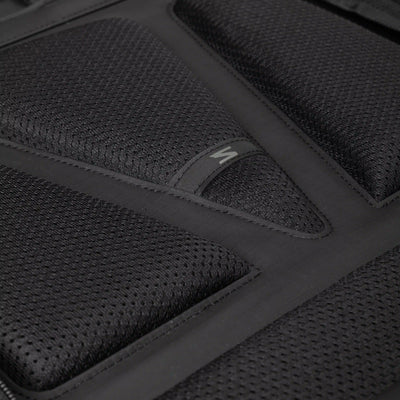 Close-up of a black textured mesh padded surface with stitched panel sections and a small white stylized logo on a black tab.