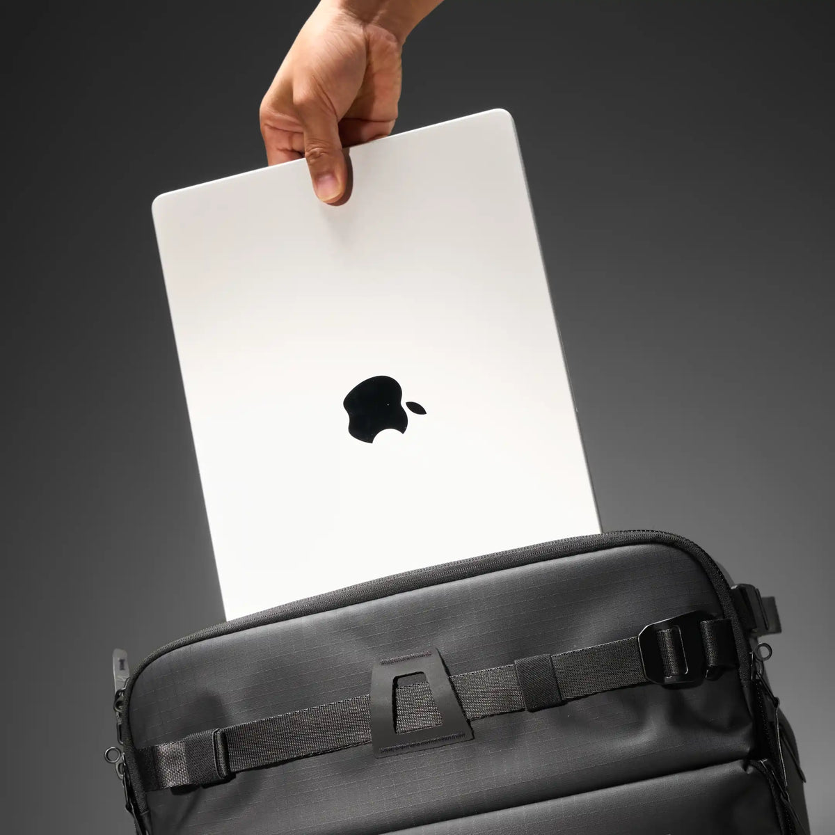 Close-up of a dark gray hard-shell suitcase handle and zipper pull on a dark gray textured bag, photographed against a dark studio background.