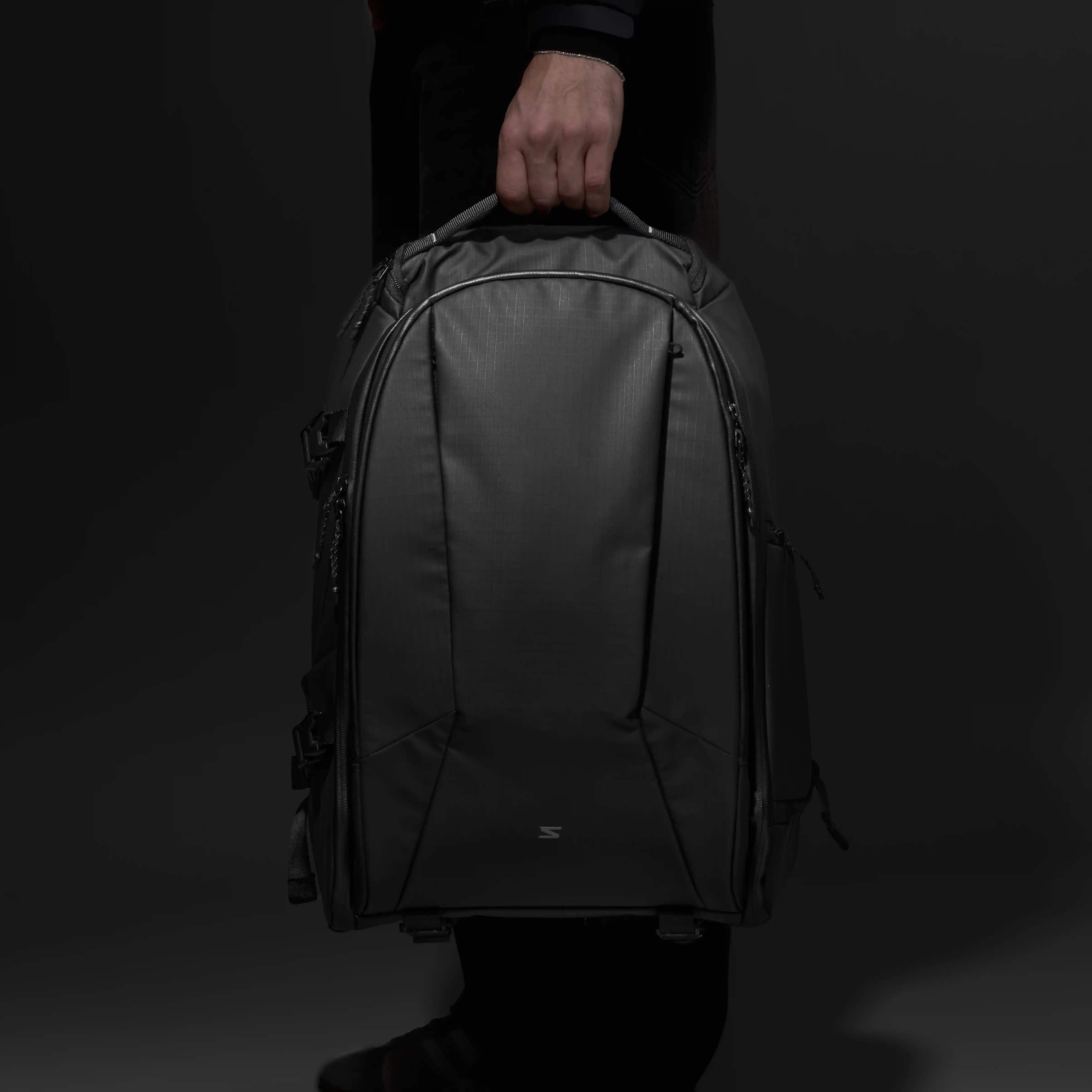 Person holding a black camera  backpack against a dark background