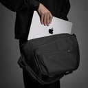 Person holding a black bag with an Apple laptop inside on a gray background