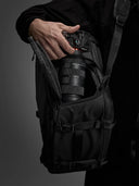 Person holding a camera with a large lens in an open black backpack against a dark background