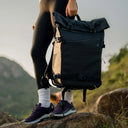 Person with a black backpack standing on a rock with a mountainous background