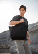 Man holding a black backpack against a rocky background