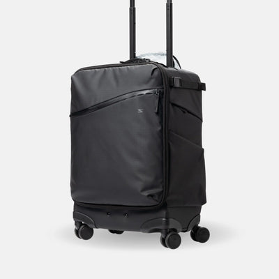 A black rolling suitcase with an extended telescoping handle, shown on a light gray studio background. The suitcase features a diagonal zippered pocket on the front, a side pocket, and four spinner wheels.