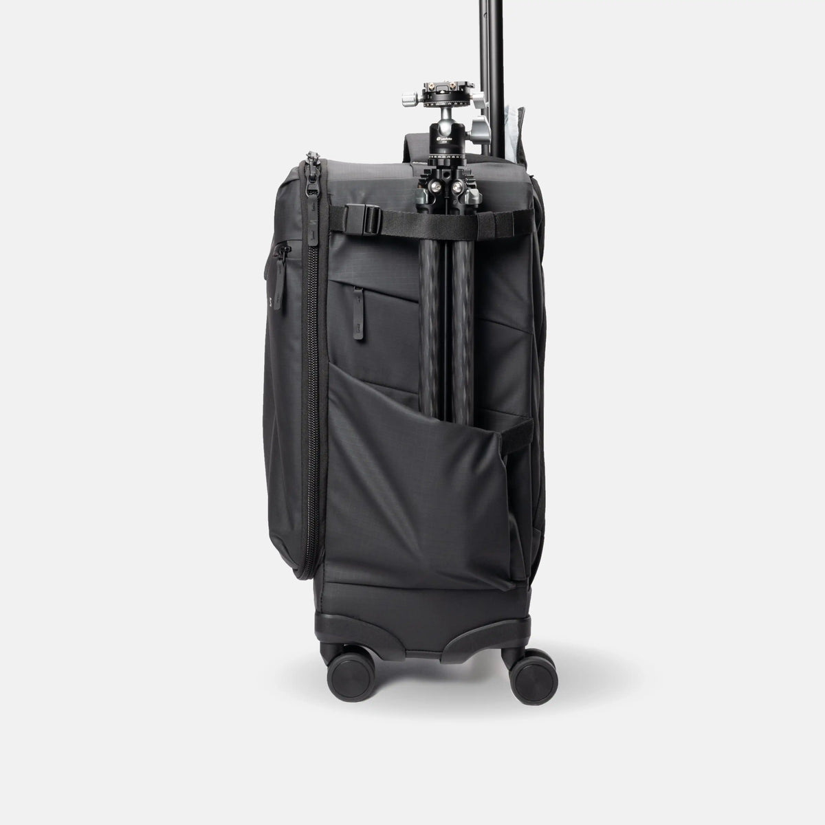 A black soft-sided travel bag with wheels and an extended telescoping handle, shown from the back with a tripod mounted on the handle wrap, against a light gray studio background.