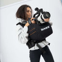 Person holding a camera with a SAKK backpack against a white background