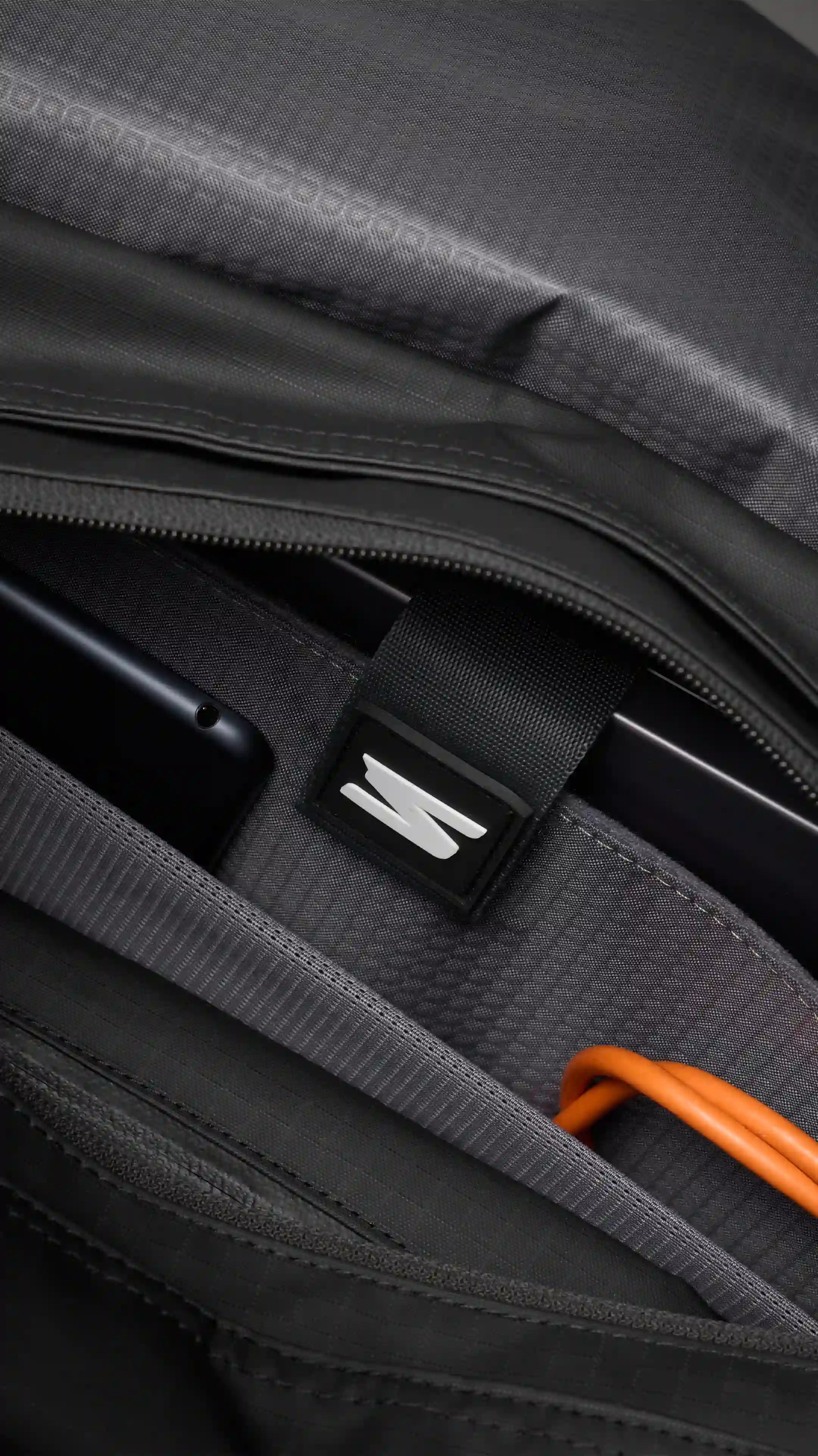 Close-up of a gray bag with a black strap and orange handle.