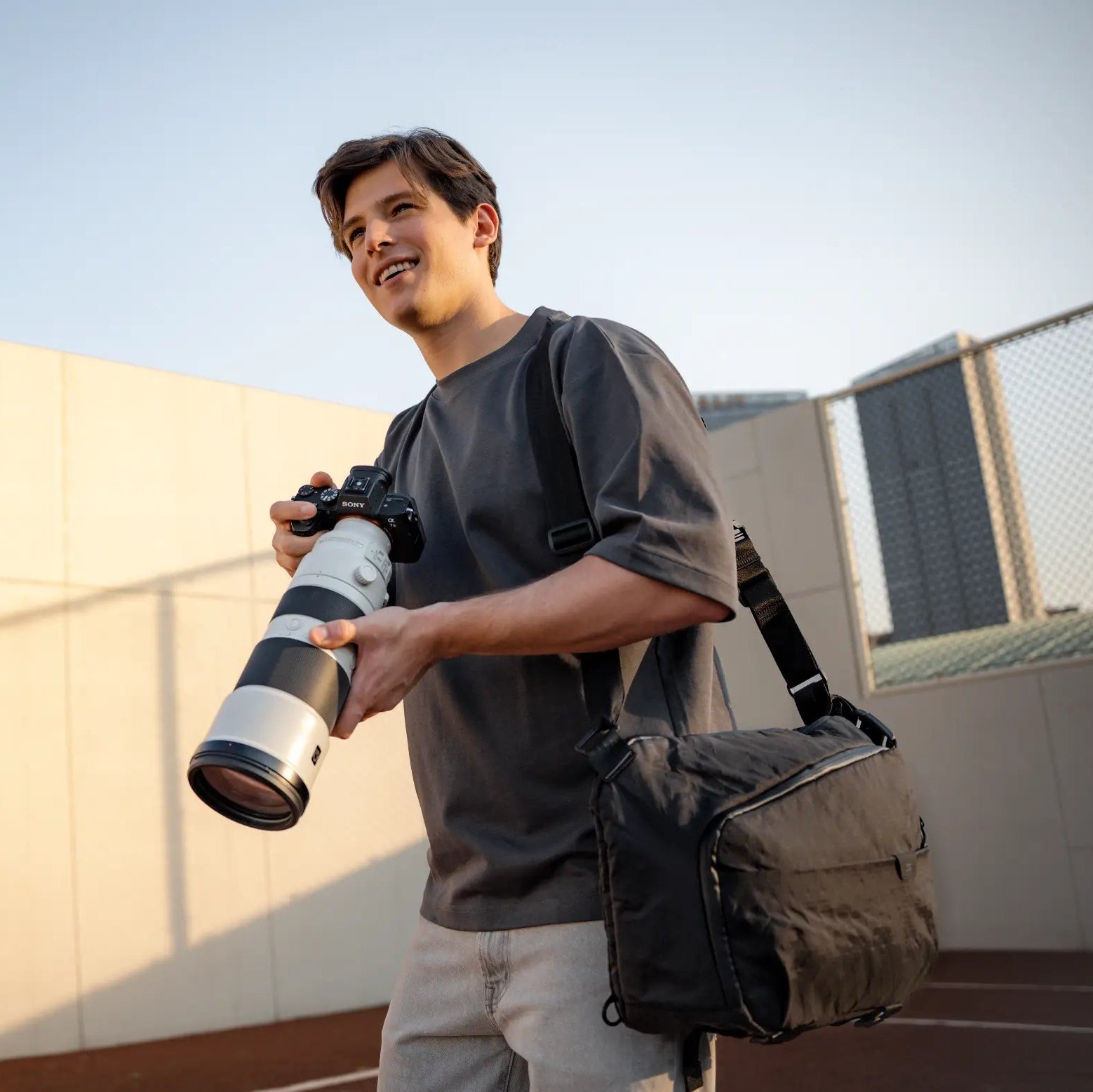 Outdoor photographer using Nomad sling bag while holding DSLR with telephoto lens. Secure compartments for gear.