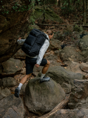 Person hiking on a rocky trail wearing a black vest and shorts.